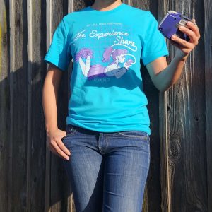 Judy models a blue Experience Share t-shirt and holds an atomic purple GBA.